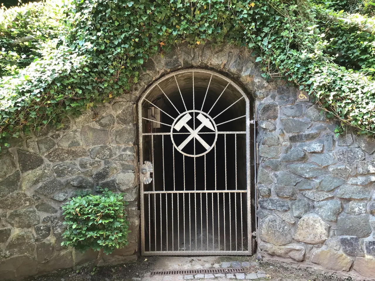 Eingangstor zum Besucherbergwerk „Finstertal“ in Schmalkalden, umrahmt von Natursteinmauer und Efeu.