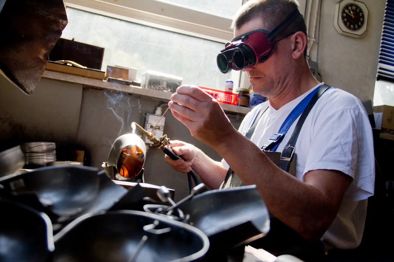 Glockengießer arbeitet mit Schutzbrille und Flamme an einer Kuhglocke in traditioneller Handwerkskunst in Kleinschmalkalden.