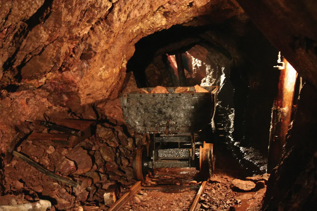 Historische Förderstrecke im Besucherbergwerk Finstertal in FSchmalkalden OT Asbach mit einem alten Förderwagen und Werkzeugen im beleuchteten Stollen.