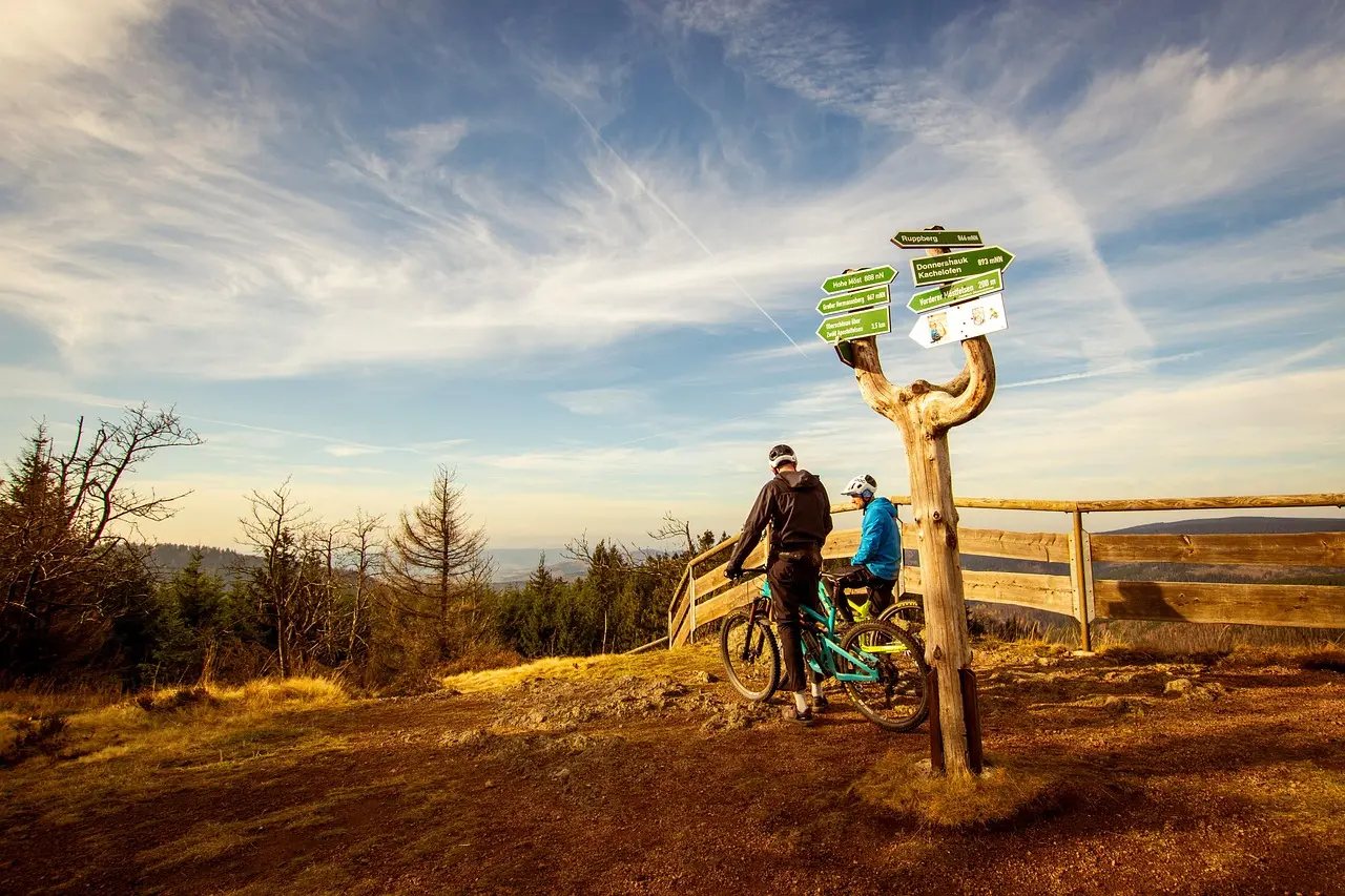 Zwei Mountainbiker am Aussichtspunkt am Rennsteig neben Wegweisern mit Blick in die Landschaft.